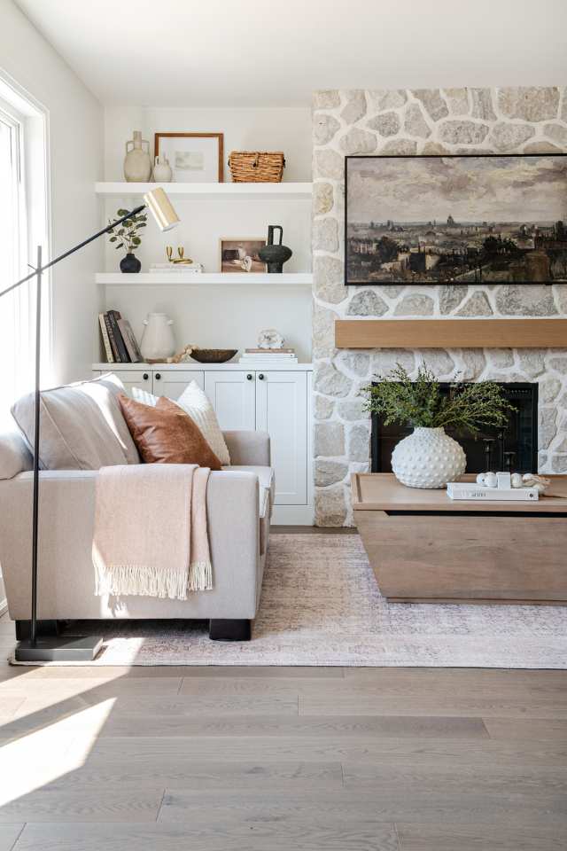 designer living room with stone fireplace, storage ottoman, and built in floating shelves